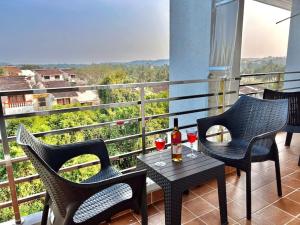 a balcony with two chairs and a table with wine glasses at Premium 2BHK Apartment with pool at Candolim Beach in Candolim