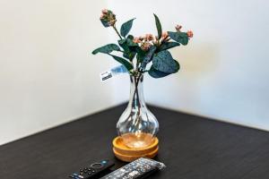 a vase with flowers on a table with two remote controls at Cozy studio for your stay in New Southgate