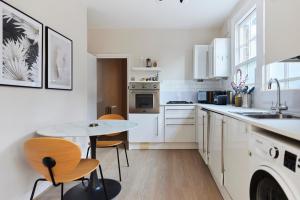 una cucina con armadi bianchi, tavolo e sedie di The Elmington Estate Place - Elegant 1BDR Flat a Londra