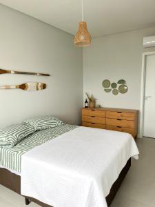 Habitación blanca con cama y tocador de madera. en Bossa Mar Apartamento, en Bombinhas