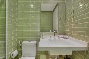 a green tiled bathroom with a sink and a toilet at Charlie NUN Itaim in Sao Paulo