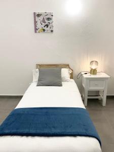 Cala Reale Rooms Marinella في مارينيلاّ: سرير ابيض مع بطانيه ازرق وقفه ليليه