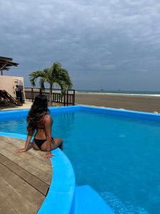 a woman sitting next to a swimming pool next to the beach at Aloha Lobitos in Lobitos