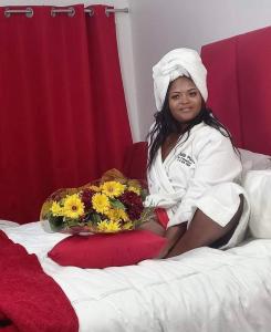 a woman sitting on a bed with a bowl of flowers at Ouklip Place Hotels in Roodepoort