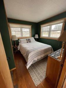 1 dormitorio verde con 1 cama y 2 ventanas en Waters Edge Cottage, en Merrimac