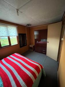 1 dormitorio con 1 cama con manta de rayas roja y blanca en Cabaña los robles, en Chonchi