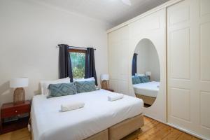 a white bedroom with a bed and a mirror at MèRose Place - Cottage on George in Bathurst