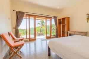 a bedroom with a bed and a chair and sliding glass doors at Ume Sari Nusa in Nusa Penida