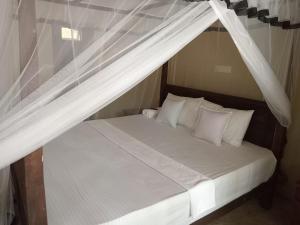 Cama con dosel con sábanas y almohadas blancas en Appu Villa, en Tangalle