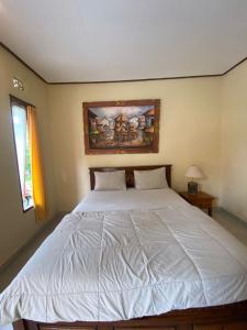 a bedroom with a white bed with a painting on the wall at MALINI Homestay in Ubud
