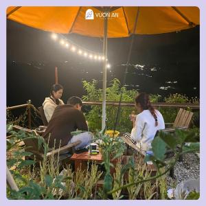 um grupo de pessoas sentadas em torno de uma mesa sob um guarda-chuva em Vuon An Villa - Best pine alley view, garden, BBQ em Ấp Ða Lợi