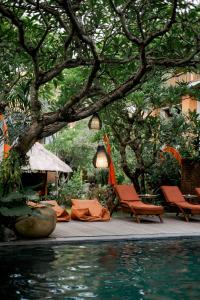 a pool with chairs and a table and a tree at Fourteen Roses Boutique Hotel, Kuta in Legian