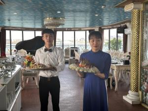 zwei Personen, die Teller mit Essen in einem Restaurant halten in der Unterkunft Halong AQUAR CRUISE in Hạ Long