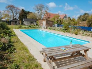 a swimming pool with a wooden table and a bench at Goosewing Hut-qu7072 in Melton Constable