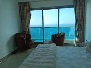 a bedroom with two chairs and a bed and windows at 30 R1 Single 1 Master Room in 3 bedroom apartment with attached washroom and balcony with fantastic sea view 30 R1 غرفة مفردة 1 ماستر في شقة 3 غرف نوم مع حمام ملحق وشرفة بإطلالة رائعة على البح in Ajman 
