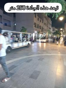 un groupe de personnes marchant dans une rue avec un bus dans l'établissement شقق جادة قباء, à Médine