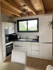 a kitchen with white cabinets and a window at CHALET ARIZONA - AU COTTAGE DU MEDOC - Proche de BORDEAUX in Saint-Aubin-de-Médoc