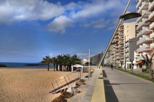 uma praia de areia ao lado de um edifício com palmeiras em Primera Linea con wifi y parking em Sant Antoni de Calonge
