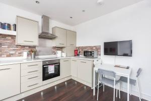 uma cozinha com armários brancos, uma mesa e uma televisão em Theodora Suite 3 - Free Parking em Kent