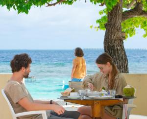 un homme et une femme assis à une table sur la plage dans l'établissement Villa Stella, Rinbudhoo, à Dhaalu Atoll