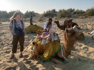 Uma mulher está ao lado de um camelo na praia. em Hotel Pol Haveli Jaisalmer em Jaisalmer
