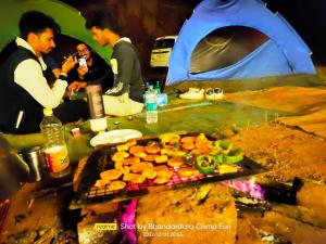 Un uomo che scatta una foto a una griglia con cibo vicino a una tenda di Bhandardara Campthrill Adventure a Bhandardara