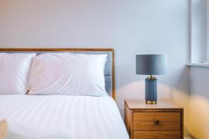 Una cama con sábanas blancas y una lámpara en una mesita de noche. en Rock Mill - Deluxe Holiday Apartments, en Stony Middleton