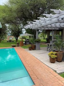 a patio with a swimming pool and a white pergola at Thabazimbi Country Lodge in Thabazimbi