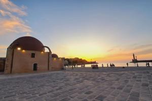 a sunset at the beach with a building and the ocean at Beautiful house in the old town of Chania- 4 rooms in Chania Town