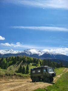 a green jeep parked on a dirt road with snow covered mountains at Roman House Borsa in Borşa
