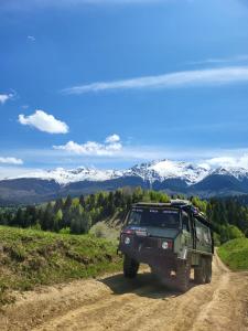 a green jeep driving down a dirt road with snow covered mountains at Roman House Borsa in Borşa