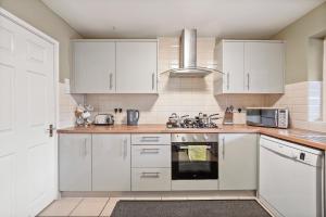 La cuisine est équipée de placards blancs et d'un four avec plaques de cuisson. dans l'établissement BridgeCity Luxurious Maidstone Holiday Home, à Kent