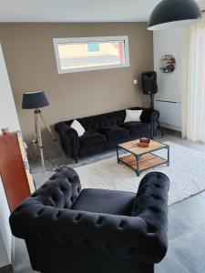 sala de estar con sofás de cuero negro y mesa en La maison des noyers, en Parigné-lʼÉvêque