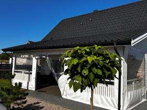 una casa blanca con un techo negro y un árbol en Domek Całoroczny Fuleda -Mazury Giżycko Sauna Jacuzii Kominek en Giżycko