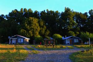 duas casas num campo com árvores ao fundo em Cabañas el Estero em Melipeuco