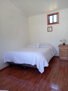 a bedroom with a white bed and a wooden floor at Alojamiento Ximena in Coñaripe