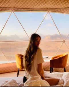 una donna seduta su un letto in una tenda di Rum Goldeneye luxury camp a Wadi Rum