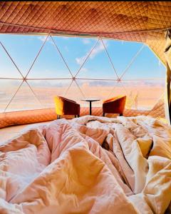 a bed in a room with a large window at Rum Goldeneye luxury camp in Wadi Rum