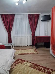 a bedroom with red curtains and a bed and a table at Micro-apartament NADEVA in Suceava