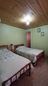 two beds in a room with a wooden ceiling at Lucerna Hostería in Curanipe