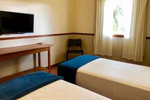 a room with two beds and a desk and a television at Obbá Coema Village Hotel in Capitólio