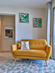 un sofá amarillo en una sala de estar con dos fotos en Charmant Appartement Topaze en Papeete