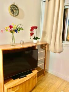 a flat screen tv sitting on a wooden stand with flowers at appartement agréable tout confort Entièrement Meublé in Aubervilliers
