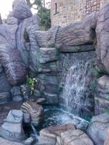 a waterfall in front of a stone wall with a fountain at Lilly's Valley Resort in Kodaikānāl