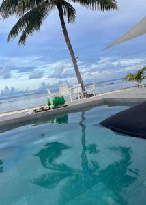 a swimming pool with a palm tree and the ocean at Pension Irivai appartement PUATOU 1 chambre bord de mer in Uturoa