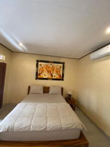 a bedroom with a white bed and a painting on the wall at MALINI Homestay in Ubud