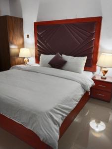 a large bed with a large wooden headboard and two lamps at Homewood Suites Family Guest House & Apartments in Lahore