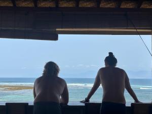 dos hombres sentados en una cornisa mirando el océano en Lakey Peak B and B en Huu