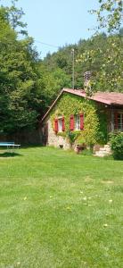a stone house with red shuttered windows in a yard at Cottage a Bossolasco con piscina in Niella Belbo