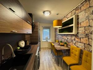 a kitchen with yellow chairs and a stone wall at Mox Downtown Apartman in Debrecen